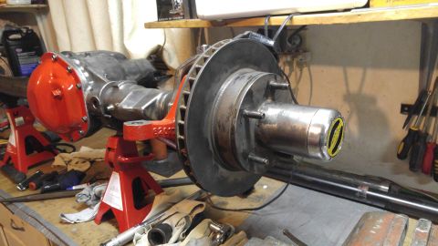1991 Ford Bronco - Close-up of a vehicle's rear axle assembly, supported by red jack stands in a workshop setting.