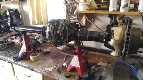 1991 Ford Bronco - A front axle assembly, possibly for a Ford Bronco, is shown on jack stands with a camouflage differential cover.