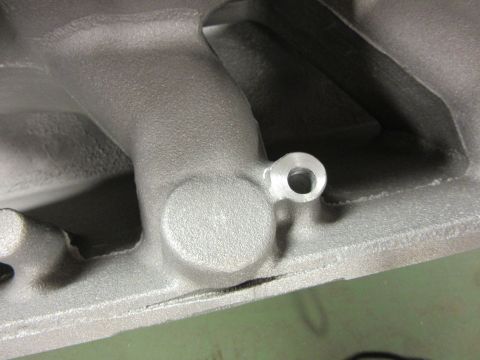 Close-up of a cast metal intake manifold with a small threaded hole