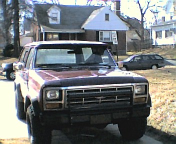 1985 Ford Bronco - A red Ford Bronco is parked in front of a house, with another car visible in the background.