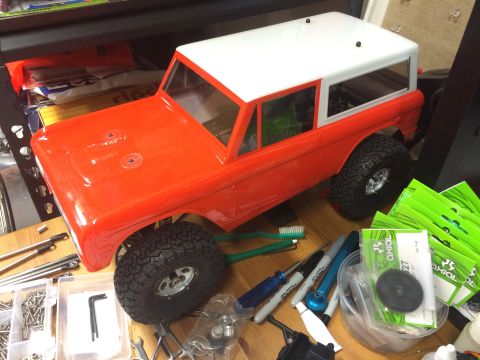 1989 Ford Bronco - An unpainted RC car body, resembling a classic SUV, is surrounded by hobbyist tools and components.