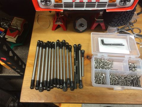 1989 Ford Bronco - A collection of RC car parts and tools are laid out on a wooden surface next to a partially assembled RC car body.