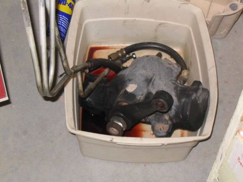 1996 Ford Bronco - Power steering gearbox soaking in fluid inside a drain pan with attached metal lines.