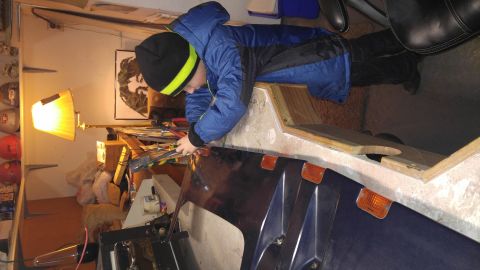 1991 Ford Bronco - A child works on a dark blue vehicle fender with orange marker lights in a workshop.