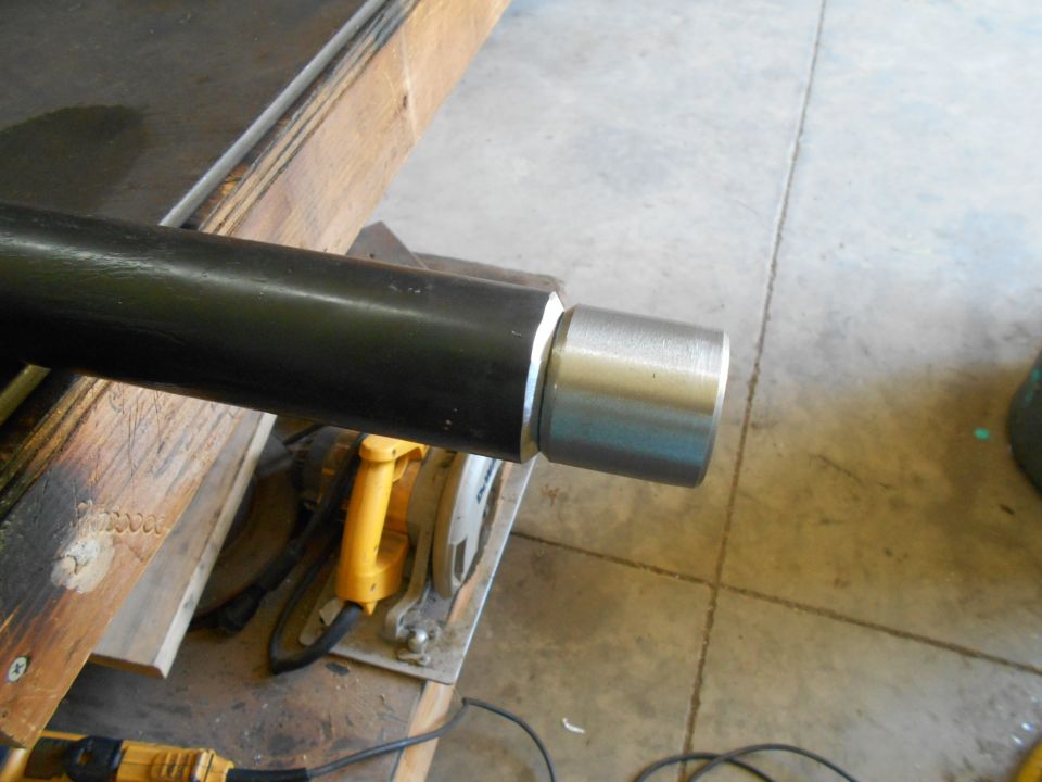 Black metal pipe with silver fitting, resting on wood near a yellow tool.