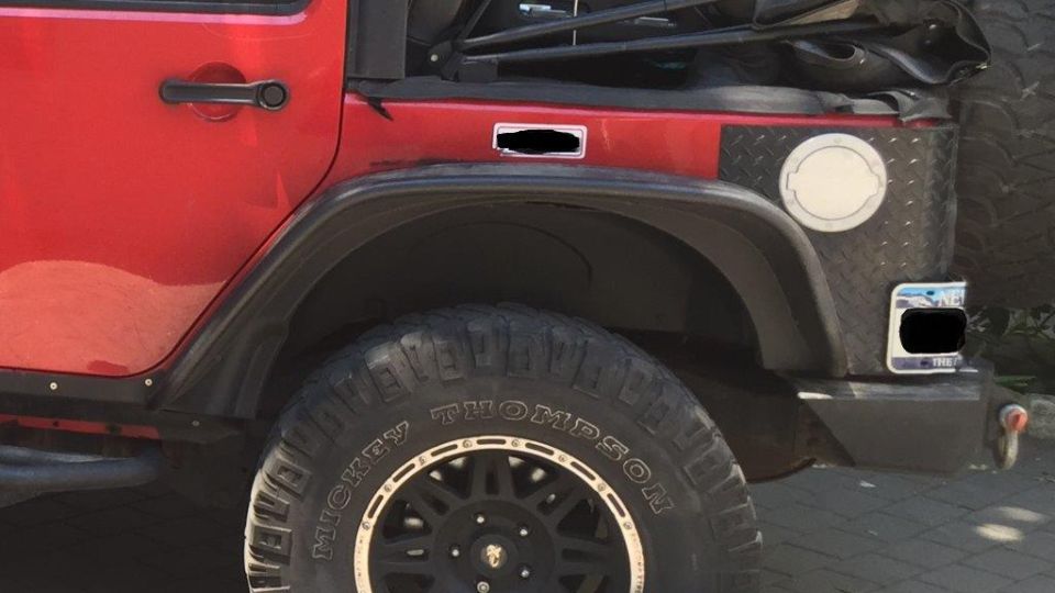 Red Jeep Wrangler rear passenger side with black fender flare, Mickey Thompson tire, and diamond plate fuel cap.
