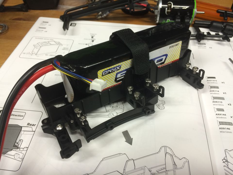 Black battery pack with wires in a black bracket on assembly instructions.