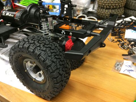 1989 Ford Bronco - RC car chassis assembly with large tires and suspension parts on a wooden surface.