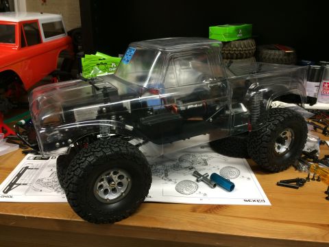 1989 Ford Bronco - A clear plastic RC truck body sits on a workbench next to an orange RC truck body, with assembly instructions visible.