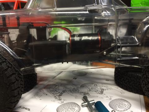 1989 Ford Bronco - Close-up of an RC car chassis, showing the motor and tires, with assembly instructions spread out underneath.