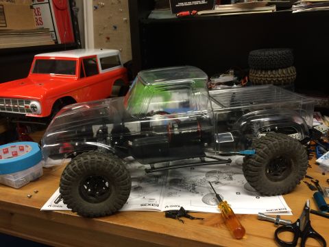 1989 Ford Bronco - An RC car chassis with a clear body sits on a workbench next to a red Ford Bronco body, surrounded by tools and assembly instructions.