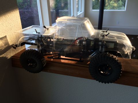 1989 Ford Bronco - RC truck with clear body and large tires sits on a wooden shelf.