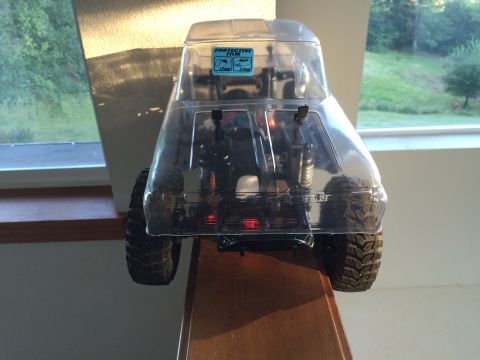 1989 Ford Bronco - Clear plastic RC car body with a protective film sticker is viewed from the rear, revealing its internal mechanics and off-road tires.