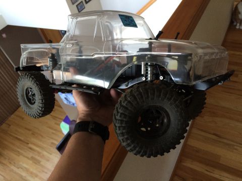 1989 Ford Bronco - A person holds a clear-bodied RC truck with large, knobby tires and visible suspension components.