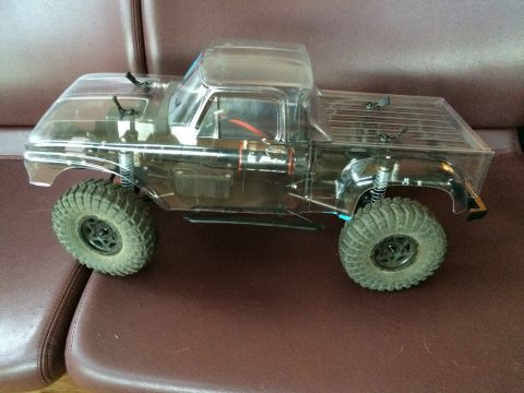 1989 Ford Bronco - Clear plastic RC truck body with large tires is shown from the side on a brown couch.