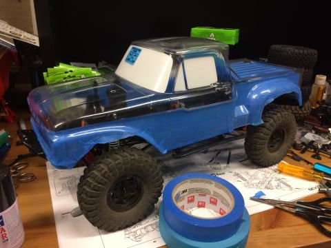 1989 Ford Bronco - RC truck body, likely a Ford F-100, is partially masked and taped in preparation for painting on a workbench.