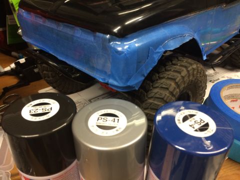 1989 Ford Bronco - RC car body is masked with blue tape, surrounded by spray paint cans in black, silver, and blue.