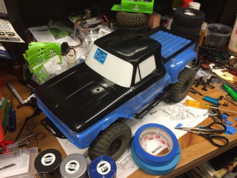 1989 Ford Bronco - An unassembled RC truck body is shown on a workbench surrounded by hobby supplies and tools.