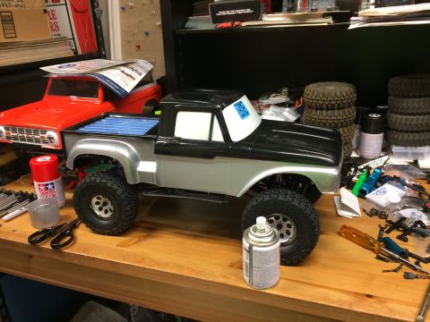 1989 Ford Bronco - RC truck body and RC Bronco body on a workbench with various tools and supplies.