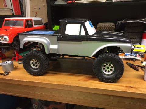 1989 Ford Bronco - A custom RC pickup truck sits on a workbench next to another RC vehicle.