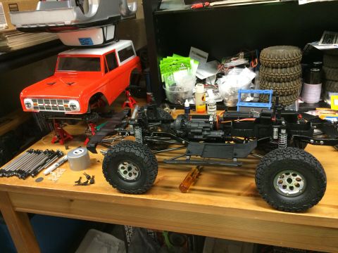1989 Ford Bronco - An RC car is partially assembled on a workbench with various parts and tools scattered around.