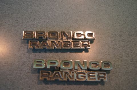 1979 Ford Bronco - Two chrome Bronco Ranger emblems are shown against a textured background.