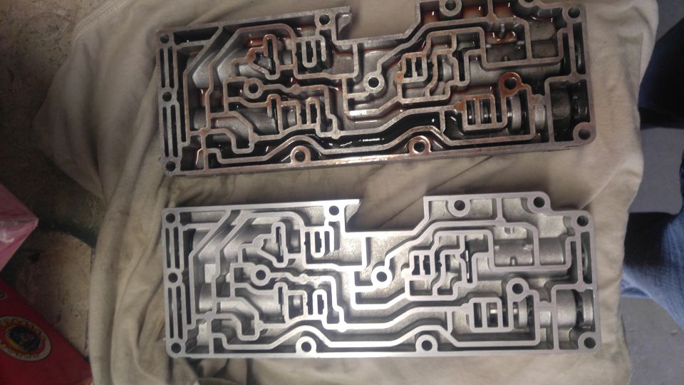 Two metal transmission valve bodies, one with dark fluid, laid out on a cloth