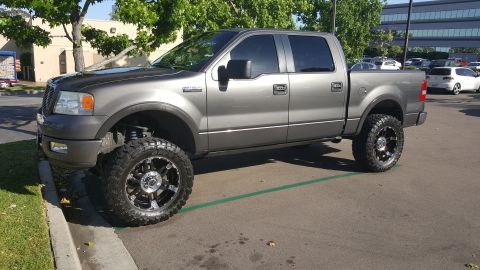 2005 Ford F-150 - A lifted gray pickup truck with custom wheels is parked in a lot.