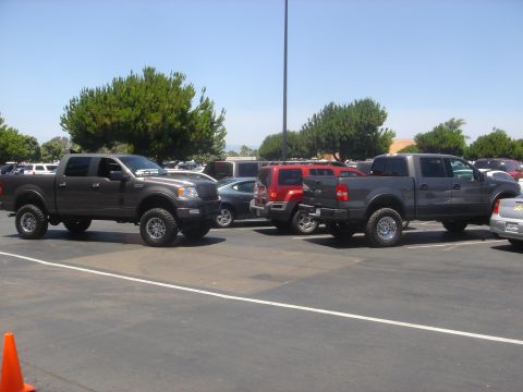 2005 Ford F-150 - Two lifted Ford F-150 trucks are parked in a lot on a sunny day.