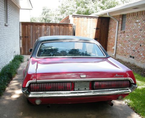 1968 Mercury Cougar - Rear view of a red 1968 Mercury Cougar parked in a driveway, its distinctive vertical taillights and chrome bumper.