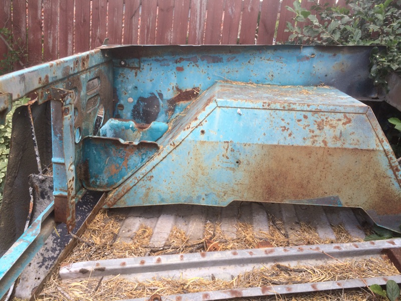 rusted blue metal car part, possibly from a truck bed or firewall area, sitting on a metal surface with straw