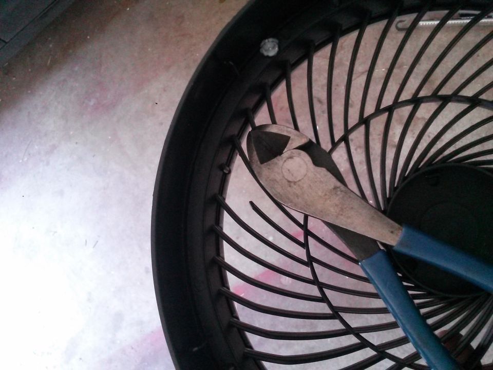 Wire cutters resting on the black plastic guard of a fan