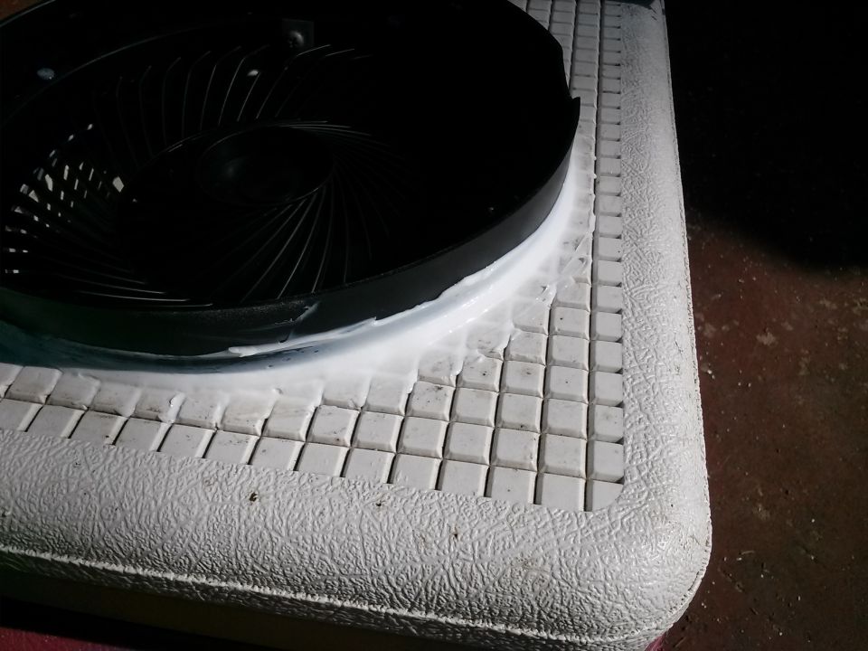 Close-up of a black fan shroud with white sealant on a textured white surface with small square tiles