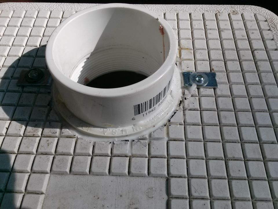 White plastic pipe fitting with barcode attached to a textured surface with a metal bracket and screw
