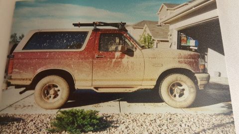 1996 Ford Bronco - Mud-covered 1996 Ford Bronco parked outside a suburban home with an open garage.