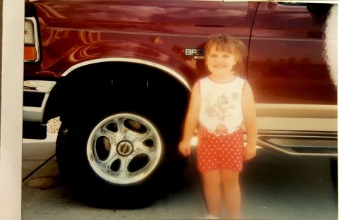 1996 Ford Bronco - A young girl poses next to a 1996 Ford Bronco, its distinctive body style and wheel design.