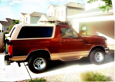 1996 Ford Bronco - A red and tan Ford Bronco is parked in a driveway with a garage in the background.