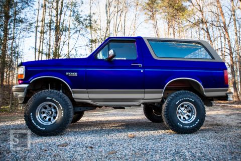 1995 Ford Bronco - A lifted 1995 Ford Bronco in a forest setting shows off its custom paint and tires.