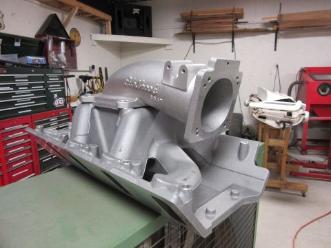 Aluminum intake manifold with "Edelbrock" text, angled view, in a workshop