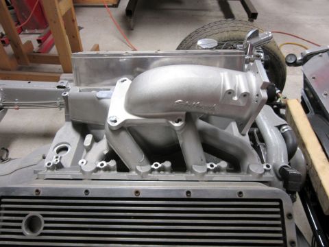 Close-up of an aluminum Edelbrock intake manifold on a V8 engine block, with a tire visible in the background