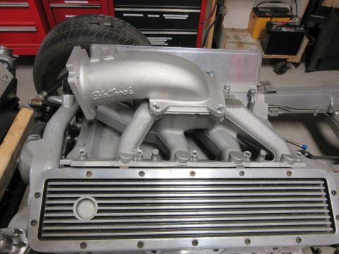 Close-up of an Edelbrock intake manifold on an engine, with a tire and toolbox in the background