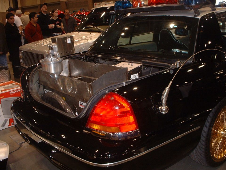 Open trunk of a black Mercury sedan fitted with custom tanks and plumbing at an indoor show