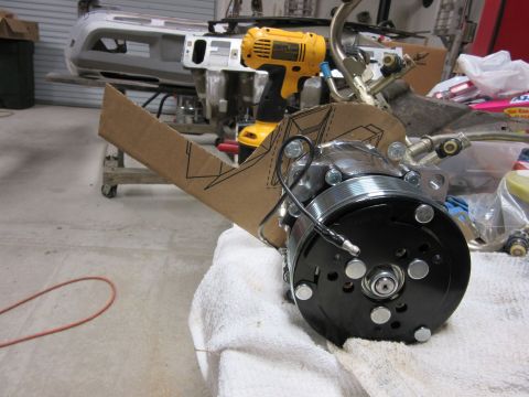 Car AC compressor with a cardboard template and a yellow drill in the background