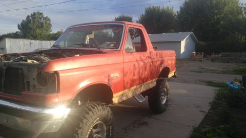 1991 Ford Bronco - This lifted Ford Bronco is parked outside a building with trees and a cloudy sky in the background.
