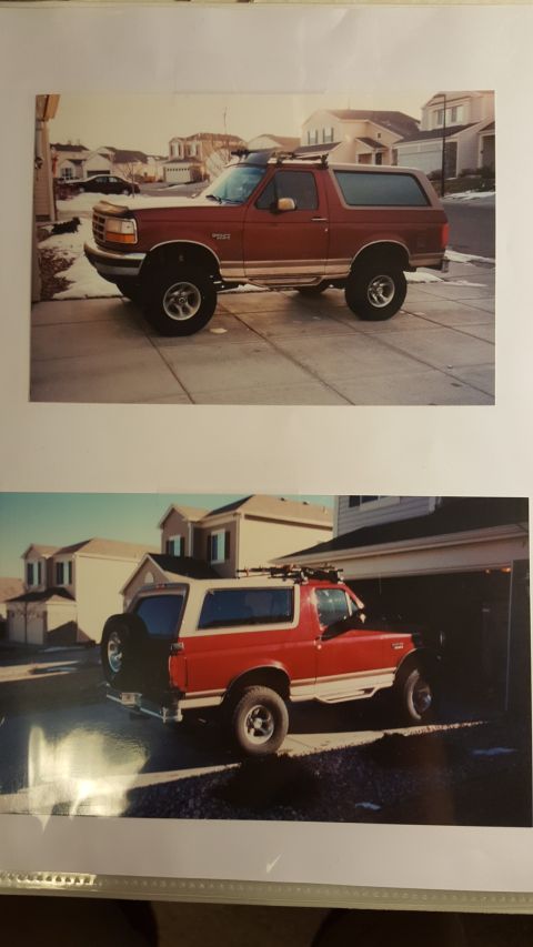 1996 Ford Bronco - A red Ford Bronco is parked in a suburban driveway, showing its side profile and roof rack.