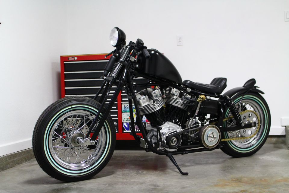 Black custom motorcycle with whitewall tires parked in front of a red toolbox