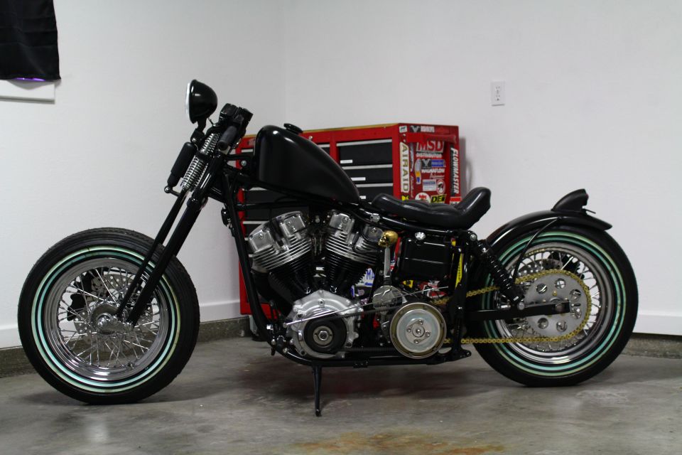 Black custom motorcycle with chrome spokes and whitewall tires parked in a garage