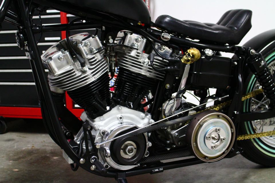 Close-up of a motorcycle engine with chrome details and a gold skull shift knob. A red and black toolbox is in the background