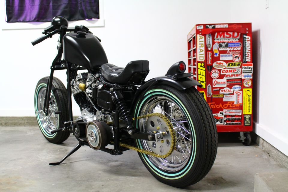 Black custom motorcycle with whitewall tires and gold chain, parked next to a red tool chest