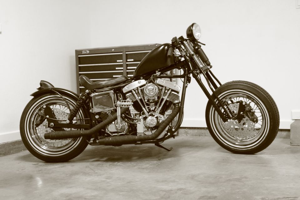Custom motorcycle with a V-twin engine, black fuel tank, and dual exhaust pipes parked in front of a tool chest